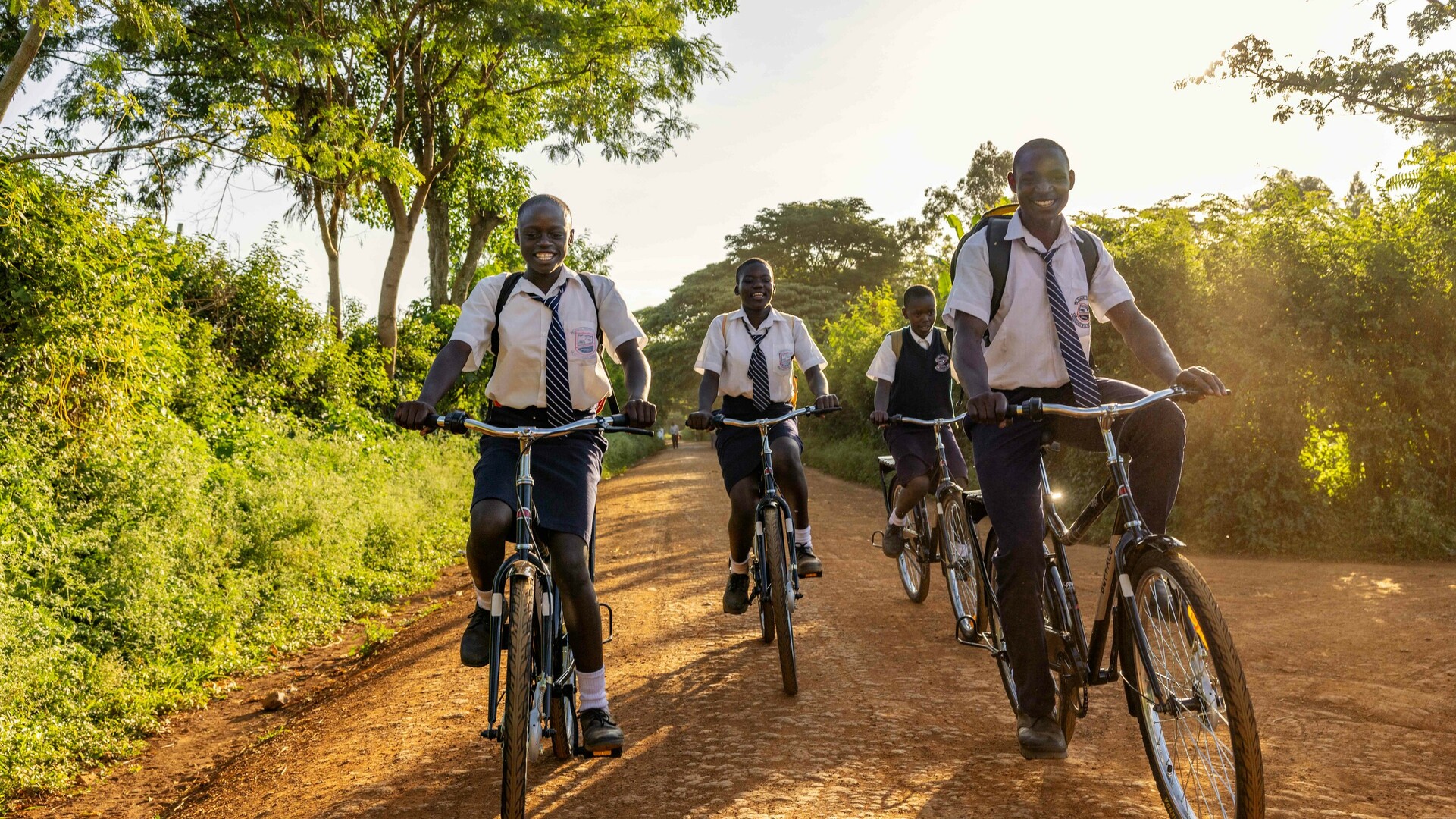 Groupe d'élèves en uniformes scolaires faisant du vélo sur une route en terre battue.