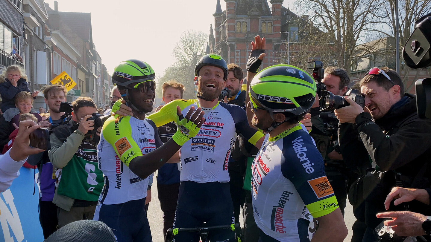 Des cyclistes sur route célèbrent à la ligne d'arrivée, entourés de photographes et de fans.